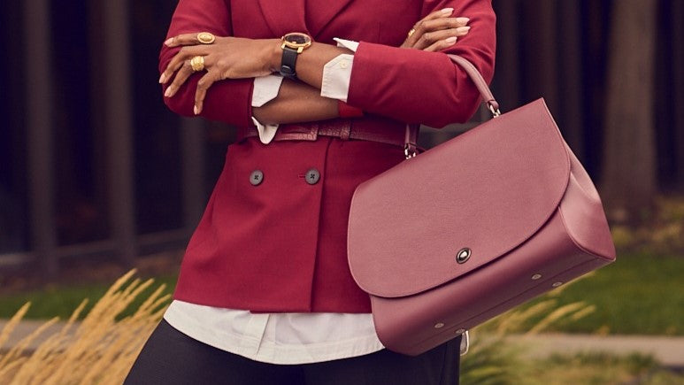 A fashion and style editorial photo showing a close-up of a woman wearing black pants with a white shirt and a belted burgundy blazer. She's holding a burgundy leather handbag.
