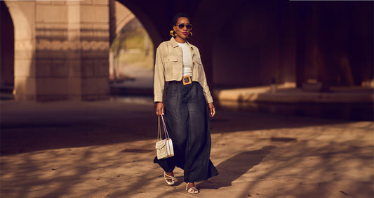 Style influencer Farotelle wearing wide-leg black pants with a fitted white tee and a cropped khaki jacket. She's also wearing sunglasses, white strappy sandals and is holding a rectangular white handbag.