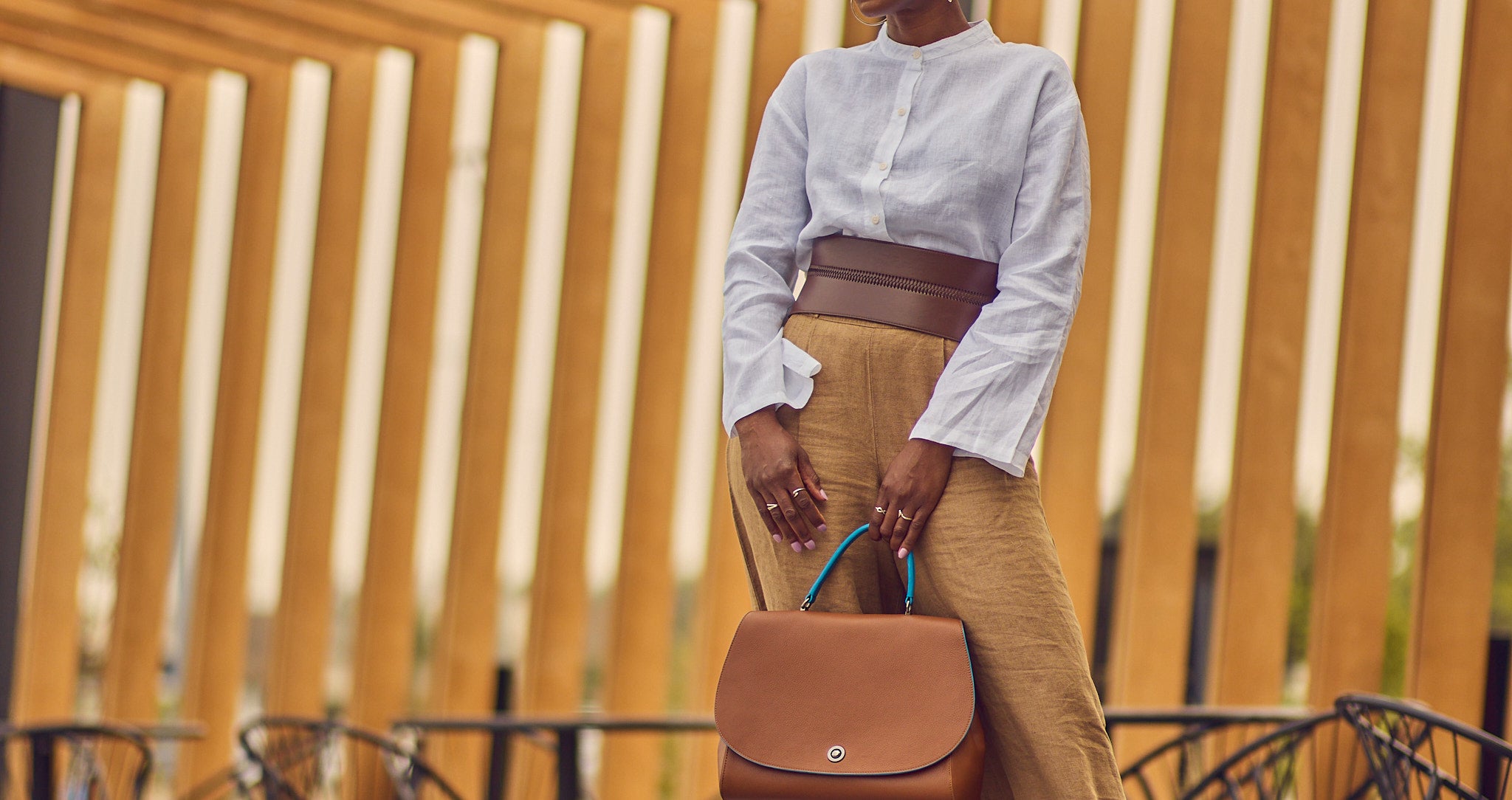 Style influencer Farotelle posing in a neutral outfit consisting of brown wide-leg pants, a white long-sleeve shirt, and a wide brown belt.